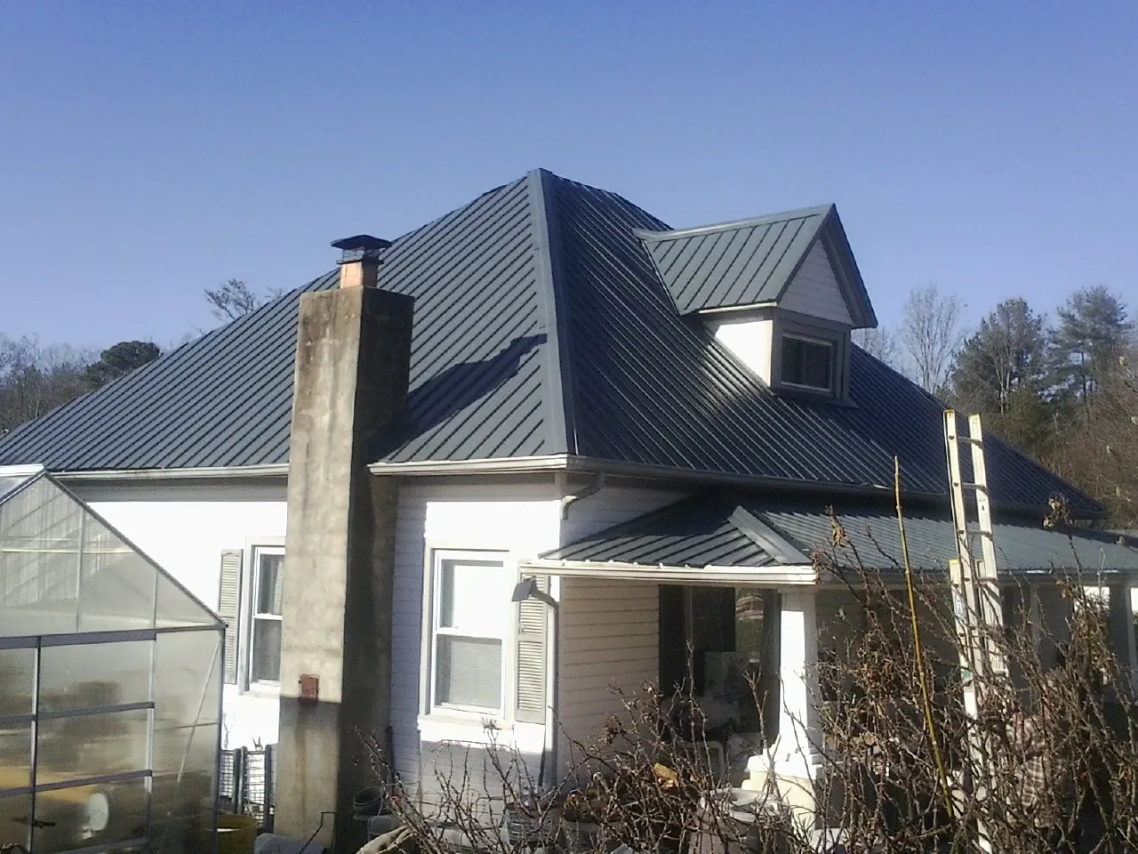 Dark blue standing seam metal roof on a white farmhouse with dormer — Slate & Tile Roof Repair by Roofing Brothers in Strawberry Point