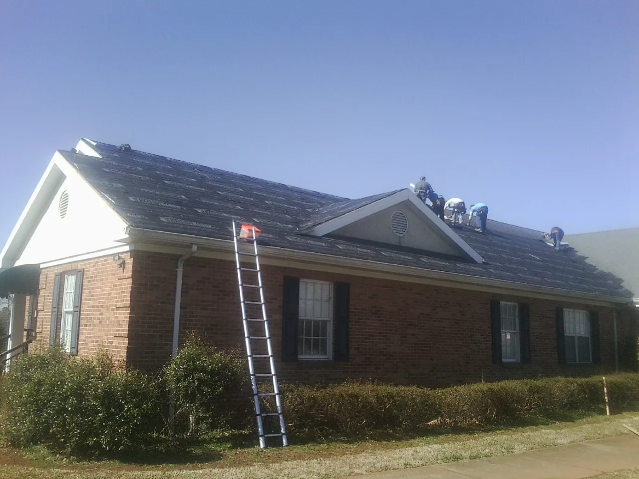 Crew tearing shingles off a brick ranch roof with a ladder set — Emergency Roof Repair work by our crew in Strawberry Point