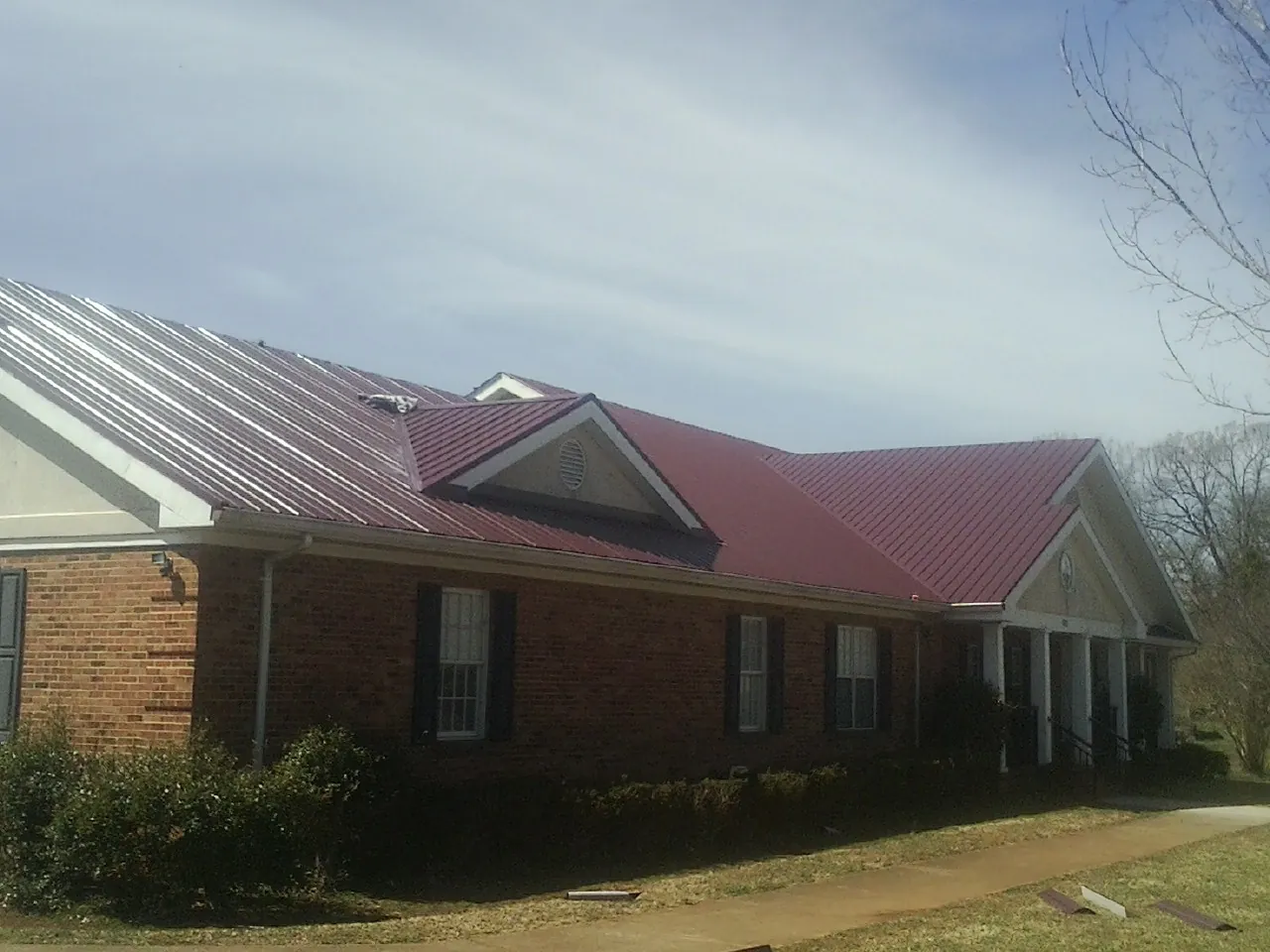 Red metal roof with gabled entries on a long brick building, from a Hail Damage Roof Repair job in Strawberry Point