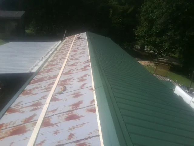 Old rusted panels beside newly installed green metal roofing — Wind Damage Roof Repair by Roofing Brothers in Strawberry Point