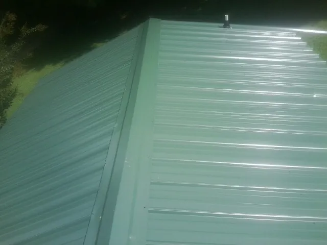 New green metal panels meeting at the ridge of a roof — Flat Roof Repair work by our crew in Strawberry Point