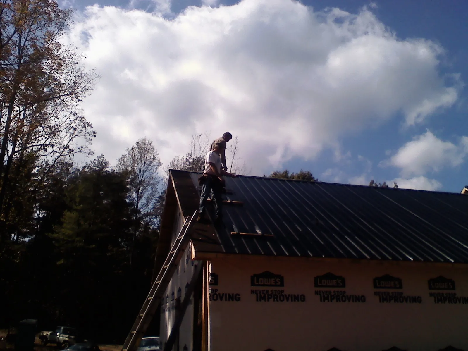 Roofer fastening dark metal panels high against a cloudy sky, from a Roof Inspection job in Strawberry Point