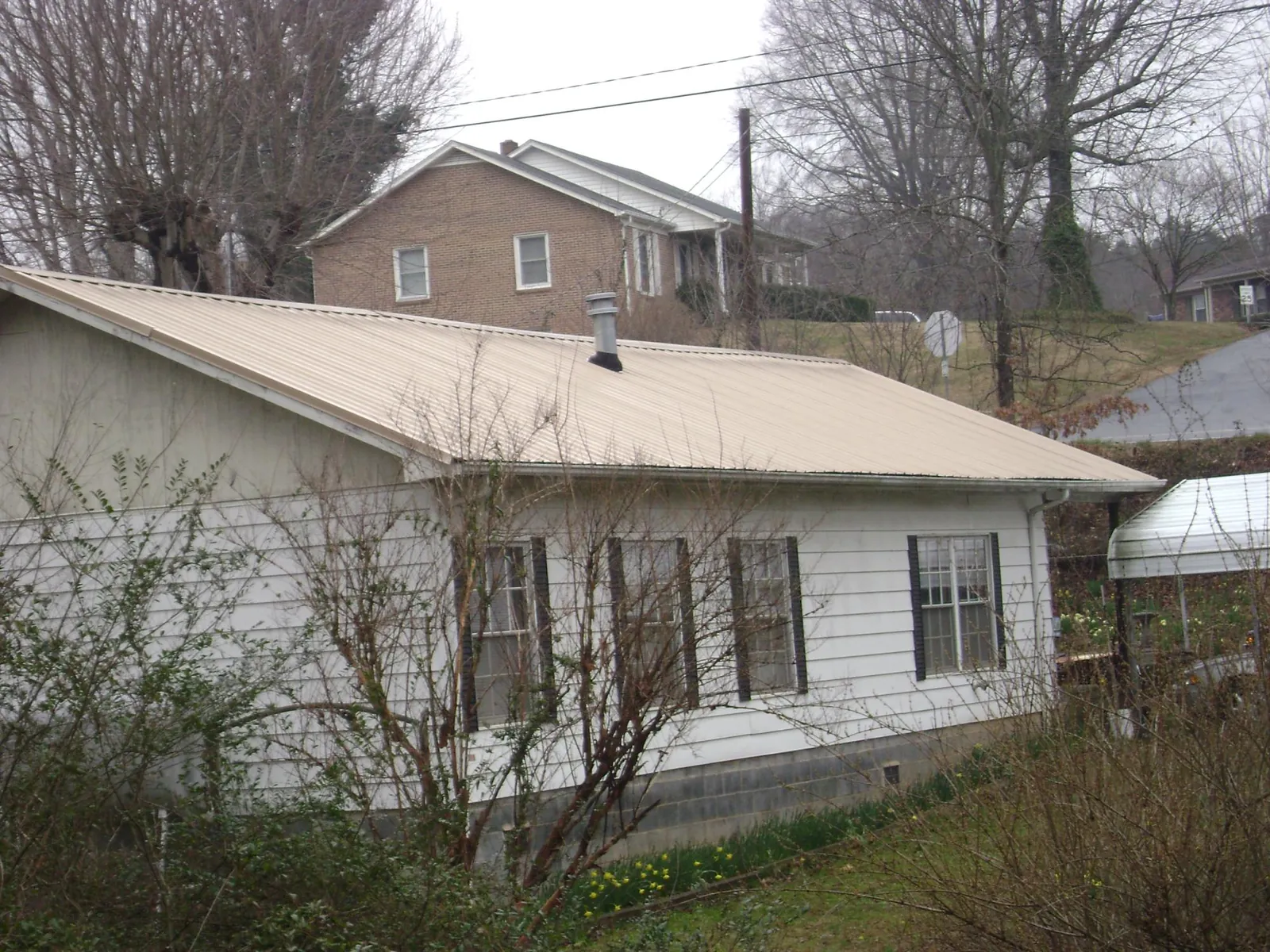 Tan metal roof on a white sided house set into a hillside — Commercial Roofing by Roofing Brothers in Strawberry Point