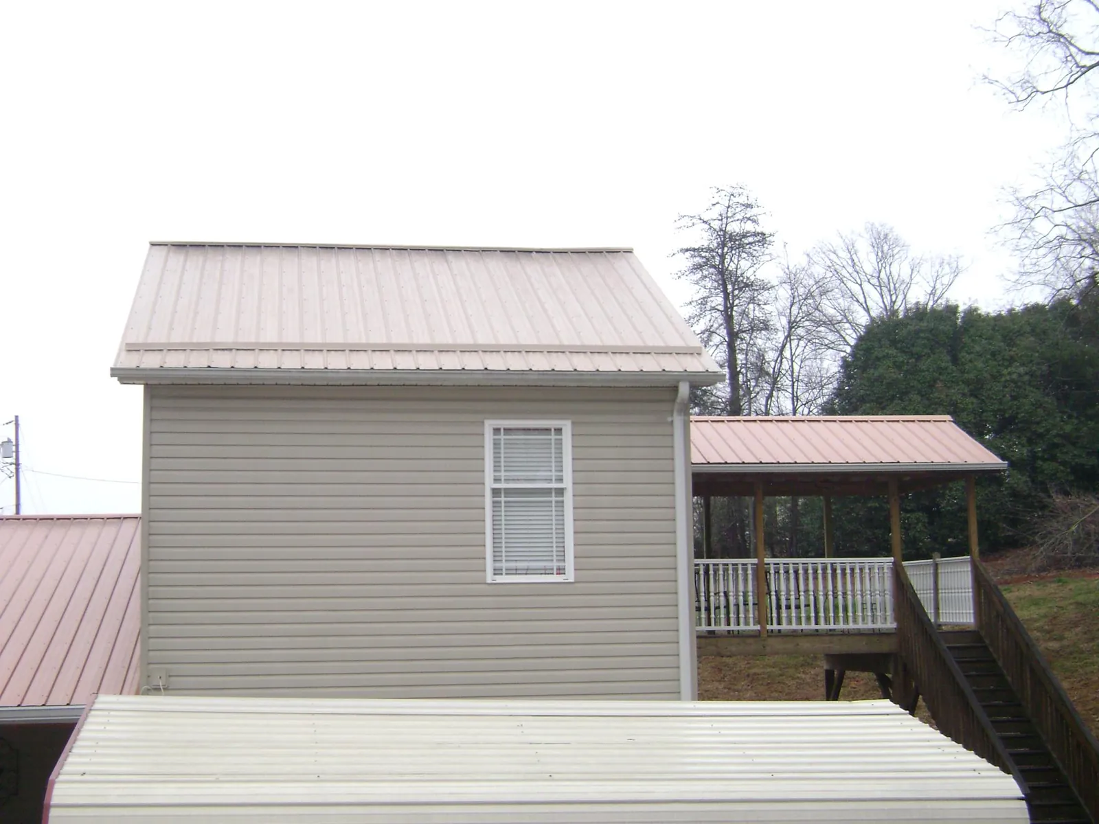 Tan metal roofs on a two story addition and attached porch, from a Roof Replacement job in Strawberry Point