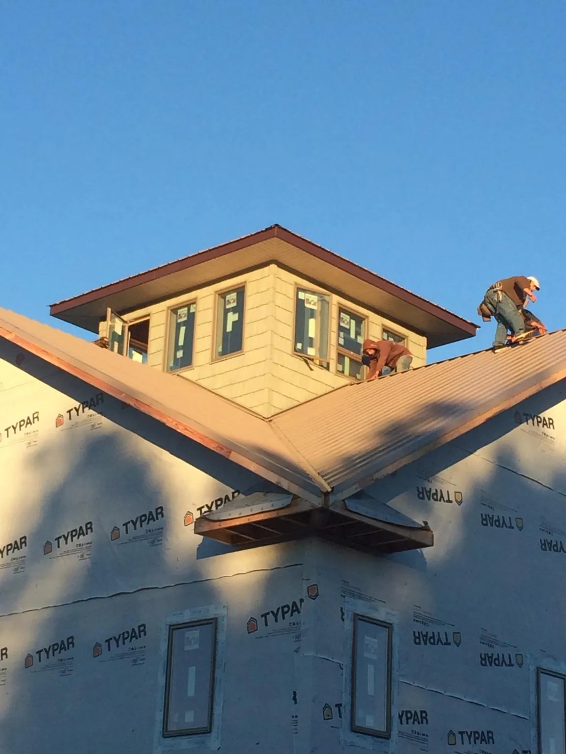 Roofers working around a rooftop cupola on a new metal roof at sunset — Roof Waterproofing in Strawberry Point by Roofing Brothers